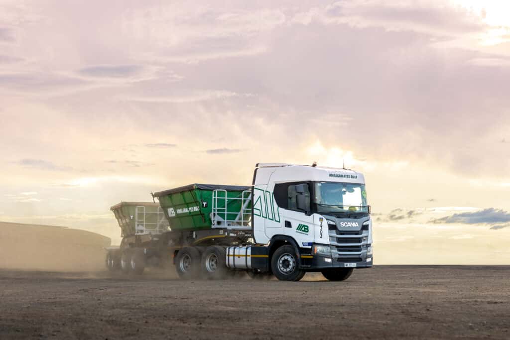 White Scania truck hauling two green trailers at sunset